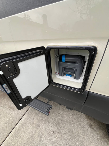 RV rental: Exterior hatch open on a cream van, revealing a grey/blue portable toilet cassette for waste disposal.