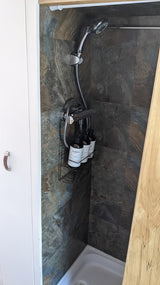 Inside an RV rental: a compact shower with dark tiled walls, a handheld shower head, and a caddy with toiletries.