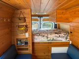 Inside an RV rental: a warm wood interior with a nature-themed bed, clever storage, and comfy blue seats.