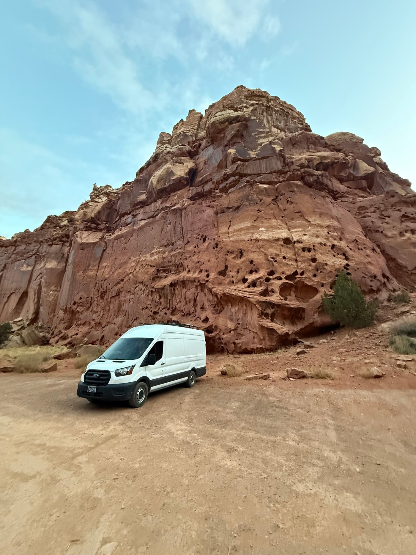  and a cascading waterfall.|White Ford Transit rv rental parked on a dirt lot at the base of a towering red rock cliff under a blue sky.|Open road adventure with an RV rental! A white camper van — photo 3