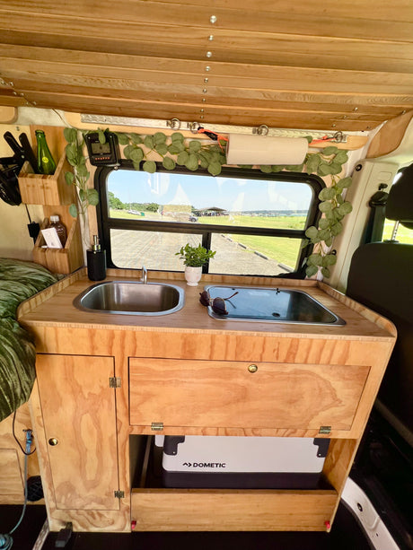 RV rental's wood kitchen: sink, stove, Dometic fridge, and a window view to nature. Ideal for adventures!