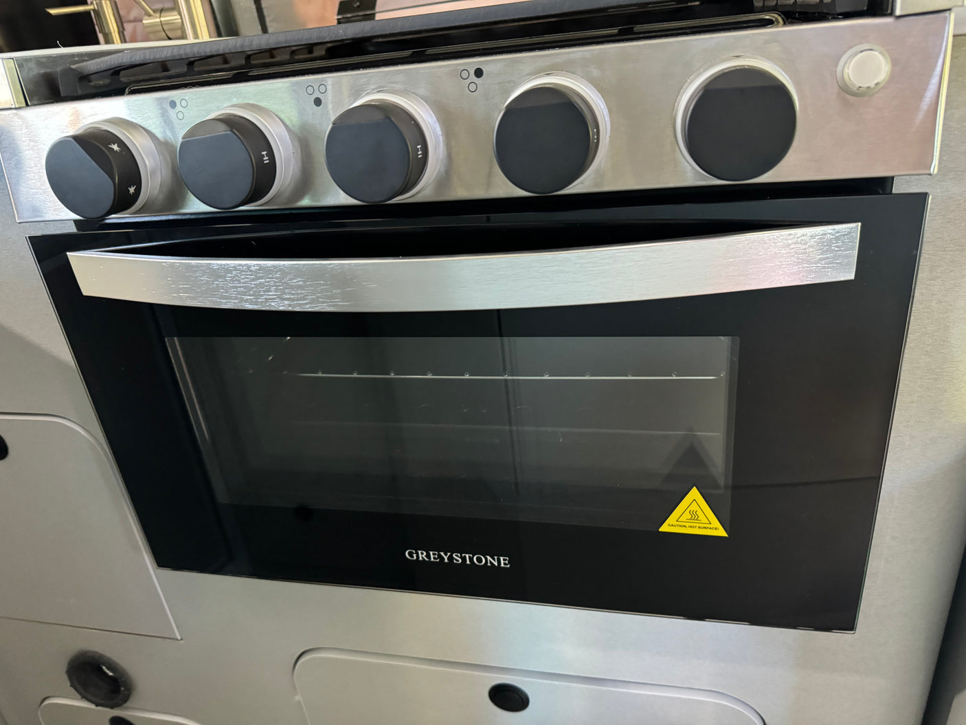 This RV rental kitchen features a stainless steel Greystone oven & stovetop with black control knobs, ready for cooking adventures.