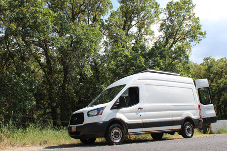 White camper van parked roadside by green trees. This RV rental is ready for scenic road trips and outdoor adventures.