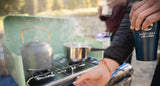 Start your day with an RV rental! Someone preps coffee on a portable stove, steam rising, holding a Moterra mug.