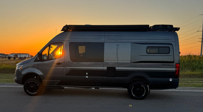  seen at sunset.|Dark grey Mercedes-Benz Sprinter camper van with a raised pop-top roof