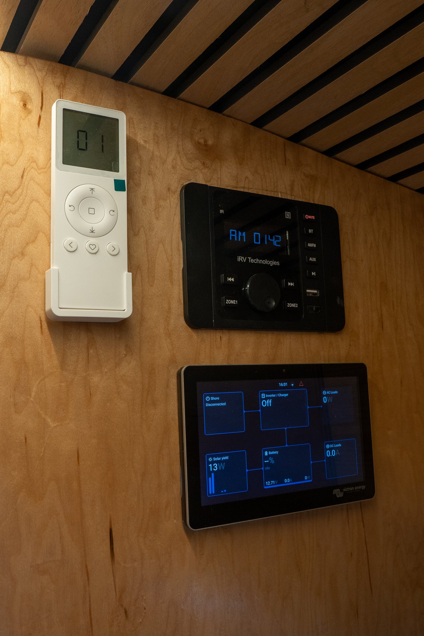 RV rental interior showing remote, iRV entertainment system (AM 01:42), and Victron energy power display (solar 13W, battery 12.71V).