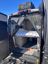 Inside an RV rental: a cozy bed with chevron bedding, pull-out storage, and a mesh bug screen at the rear. Ready for adventure.