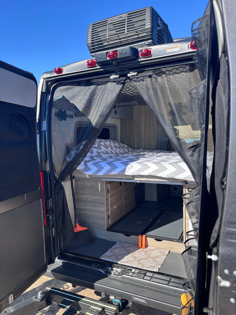 Inside an RV rental: a cozy bed with chevron bedding, pull-out storage, and a mesh bug screen at the rear. Ready for adventure. — photo 10