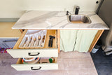 Compact RV rental kitchen with marbled counter, sink, and organized drawers for utensils and dishes.