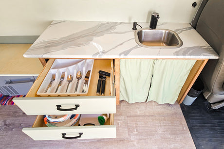 Compact RV rental kitchen with marbled counter, sink, and organized drawers for utensils and dishes.