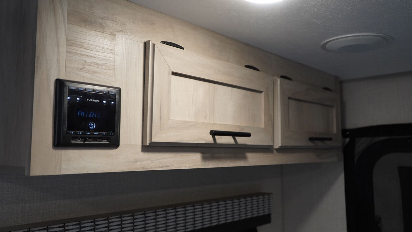 RV rental interior featuring light wood overhead cabinets, a Furrion stereo with FM 104.1 display, and a ceiling speaker.