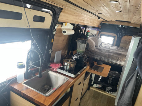 Spacious RV rental interior with a wooden kitchen (sink, cooktop, blender) and comfy bed. Ideal for van life adventures.