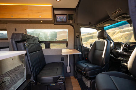 An inviting RV rental interior showing passenger seats, a removable table, and a touchscreen control panel for comfortable travel.
