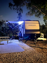 Enjoy a peaceful night camping! This illuminated Winnebago travel trailer RV rental sets the scene at a quiet campsite.