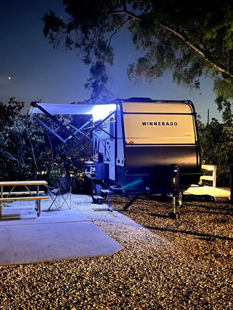 Enjoy a peaceful night camping! This illuminated Winnebago travel trailer RV rental sets the scene at a quiet campsite.