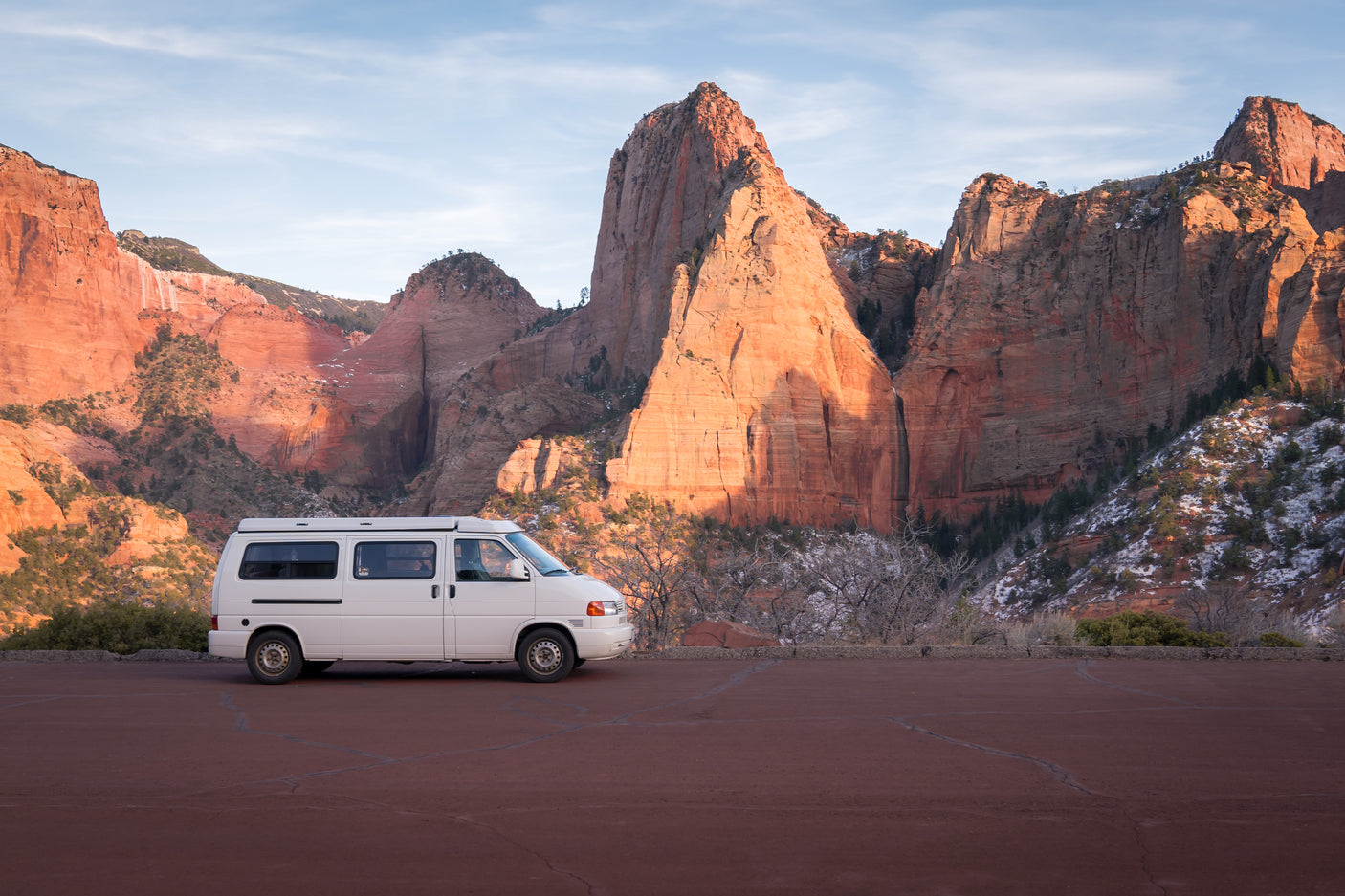 White RV rental van at a scenic viewpoint, with majestic red rock formations of Zion National Park in the background.