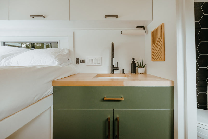 RV rental: Modern van interior featuring a compact kitchen with green cabinets, wood counter, and cozy bed area. — photo 6