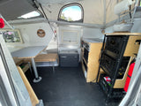 Pop-top RV rental interior showing dining table, Dometic fridge, and a compact kitchen with storage and fire extinguisher.