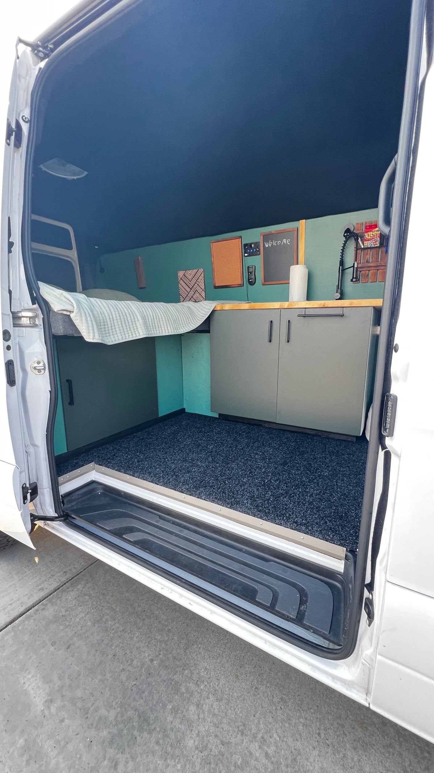 Spacious RV rental camper van interior: cozy bed, kitchen counter, ample storage, and dark blue floor.