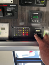 Monitoring an RV rental's systems: A hand presses a tank test button on a control panel displaying battery voltage (13.6V), generator hours (146.3), and tank levels.