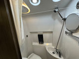 A pristine RV rental bathroom, showcasing a compact shower, toilet, sink, and wall-mounted dispensers.