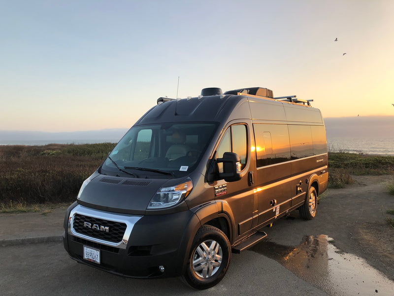 Golden hour reflects on a modern RV rental camper van, parked by the ocean with coastal plants and birds. — photo 1