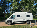 White Winnebago Solis rv rental van parked at a sunny campsite with utility hookups.
