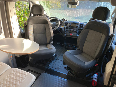 RV rental interior: Front cabin with driver/passenger seats, dashboard, a table, and fire extinguisher.