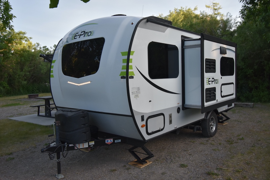 A white and gray E-Pro travel trailer, perfect for an rv rental, is parked at a campsite with its slide-out open. — photo 5