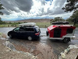 Ready for adventure! A dark minivan with roof cargo box tows a red teardrop RV rental camper, perfect for camping travel at a national park.