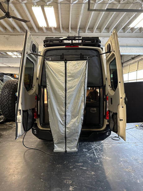 Overland van RV rental: Rear view with open doors shows interior storage & a deployed fabric privacy awning.