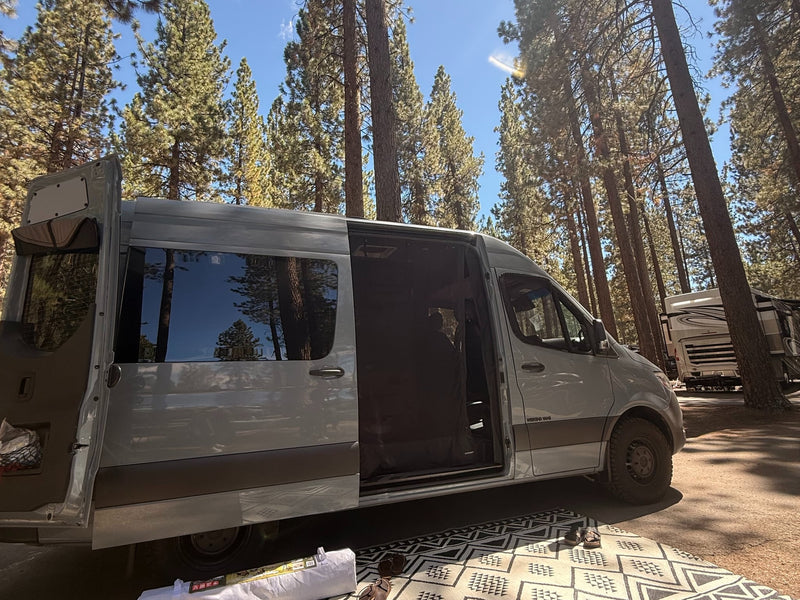  looking towards the dashboard and outside view of trees and houses.|This RV rental's Mercedes-Benz van interior features a modern cockpit with a steering wheel — photo 6