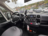 Dashboard & driver's seat of an rv rental campervan. View out to a busy parking lot, coastal houses, and palm trees.