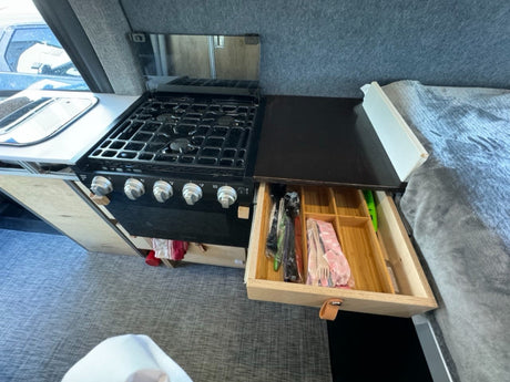 Compact rv rental kitchen featuring a stove, sink, and an organized pull-out drawer with utensils.
