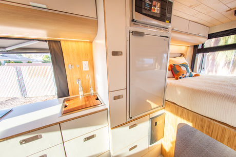 Bright RV rental interior: integrated kitchen with sink, microwave, fridge, and a comfortable bed.