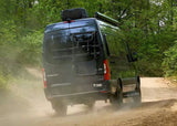 A Thor "Tranquility" Mercedes Sprinter RV rental kicks up dust on a forest trail, ready for off-road adventures.