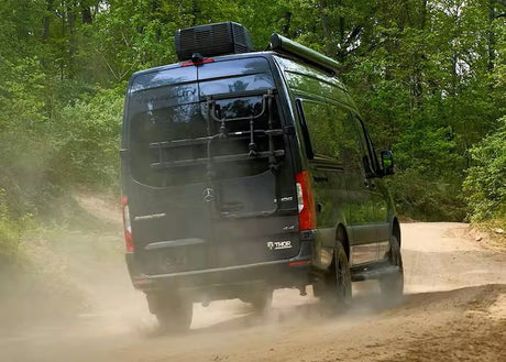 A Thor "Tranquility" Mercedes Sprinter RV rental kicks up dust on a forest trail, ready for off-road adventures.