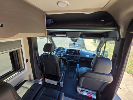 RV rental: Mercedes-Benz campervan interior showing cockpit, front seats, and overhead bunk.