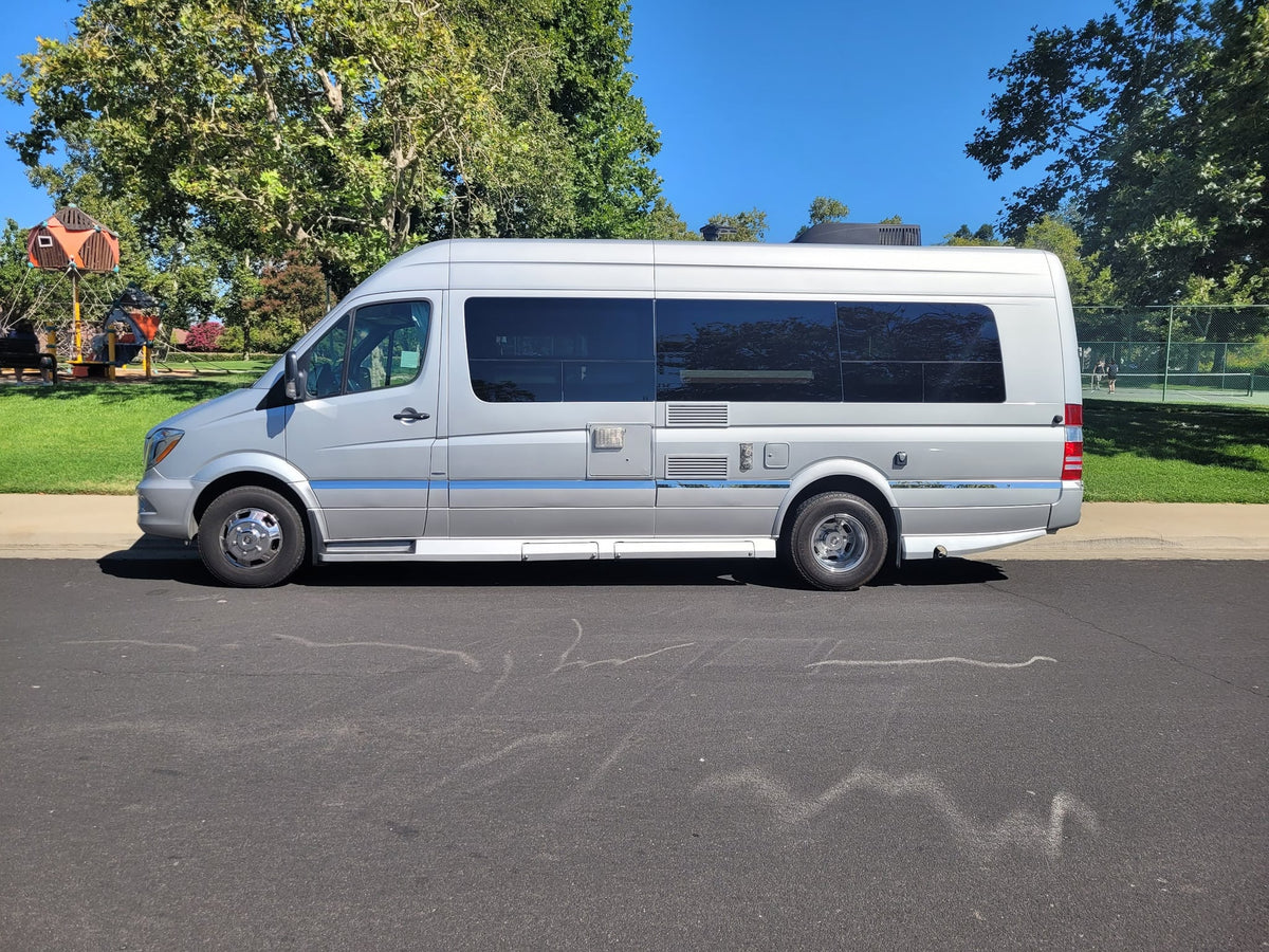  seen parked on a sunny street.|Silver RV rental parked on a sunny day. A park with a playground and tennis courts is visible nearby.|Comfortable cream captain's chairs inside an RV rental. Explore mobile living with this well-appointed camper van interior.|RV rental interior: Looking towards the back — photo 8