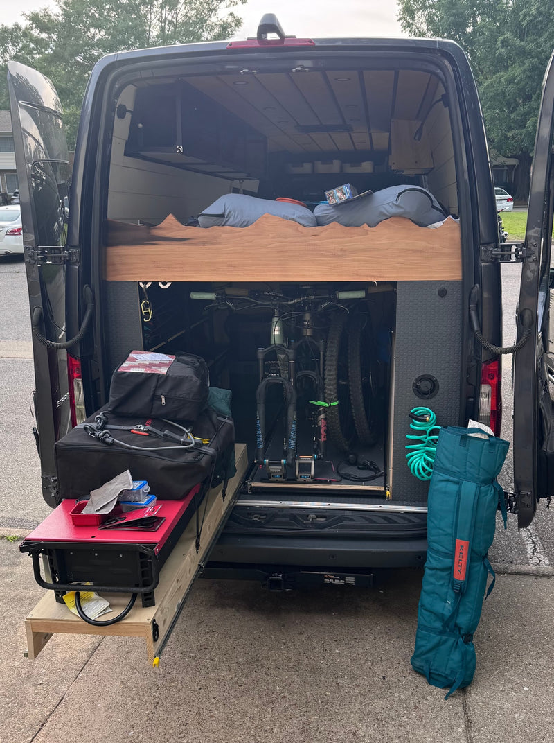 RV rental: Inside a camper van, showcasing mountain bikes, a bed platform, pull-out table, and outdoor gear in the rear storage. — photo 8