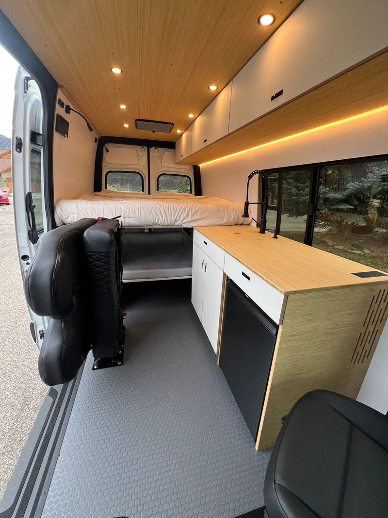 Modern **rv rental** camper van interior with wood paneling, kitchenette, bed, and flexible seating on textured grey flooring. — photo 11