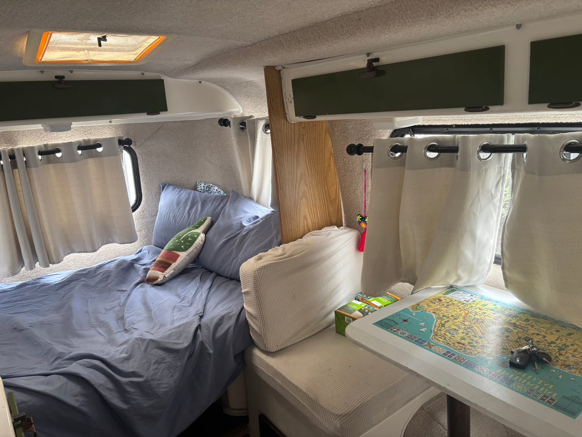 Inside a compact rv rental: a comfy bed, small dinette with a map, overhead storage, and light curtains. — photo 5