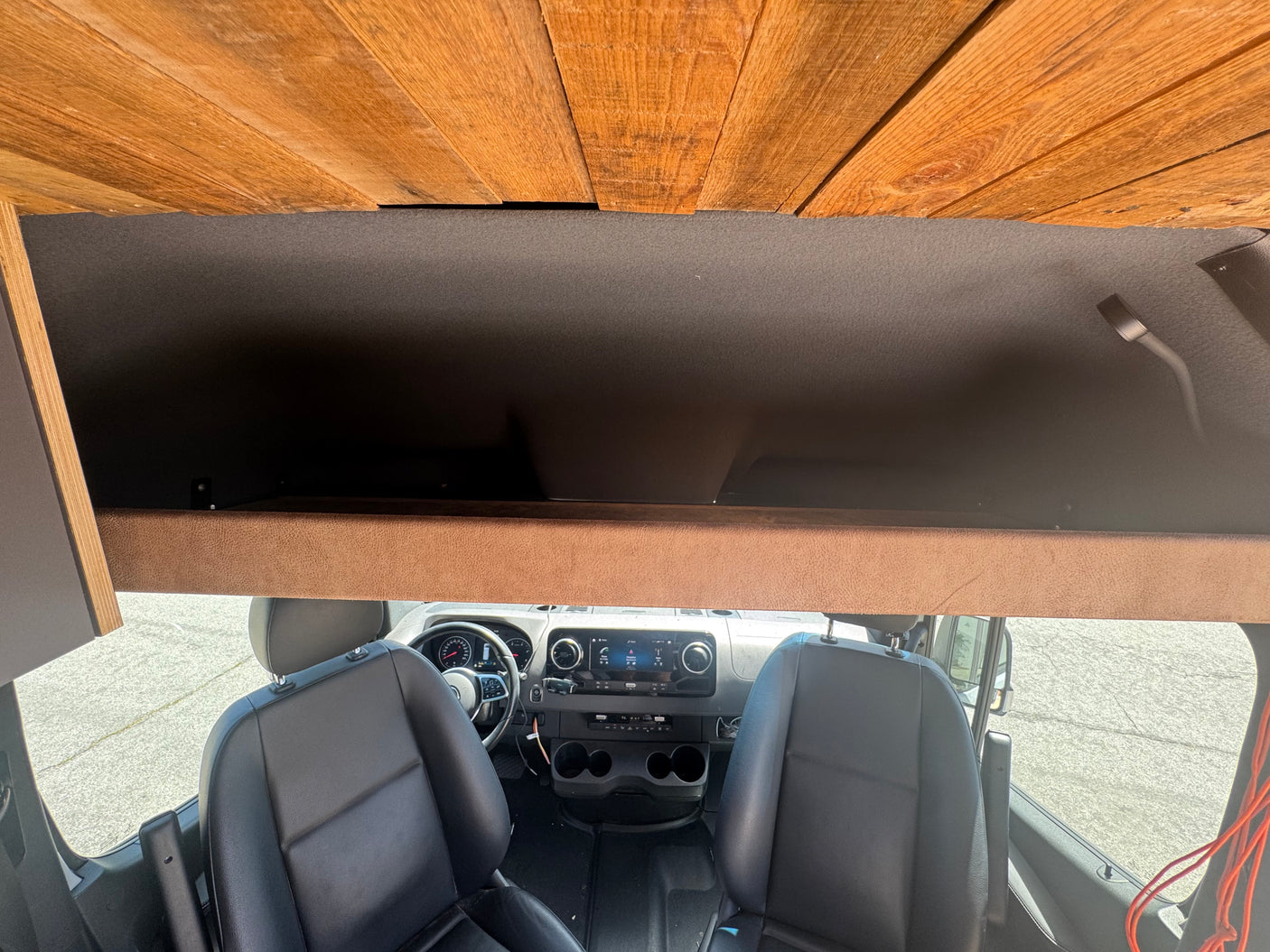 RV rental camper van's front interior, showcasing black seats, dashboard, an overhead storage compartment, and a plank wood ceiling.