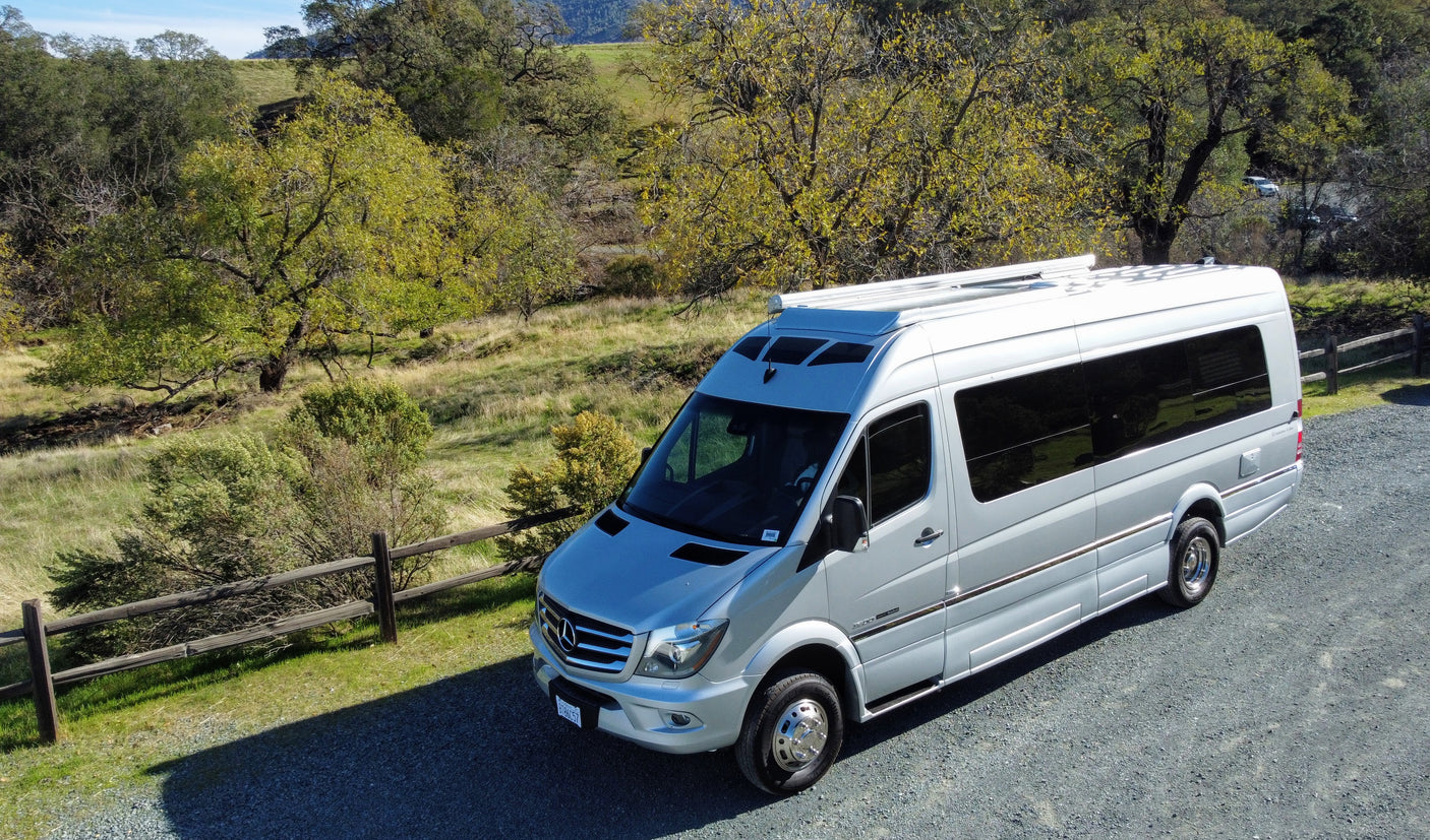 Silver Mercedes Sprinter camper van for RV rental, parked in a scenic, sunny landscape.