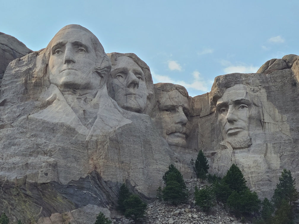Explore Mount Rushmore with an RV rental! Four presidential faces carved into the rock under a blue sky.