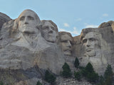 Explore Mount Rushmore with an RV rental! Four presidential faces carved into the rock under a blue sky.