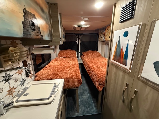  set up with outdoor chairs and a patterned mat for camping.|Cozy rv rental interior featuring two comfortable beds — photo 2