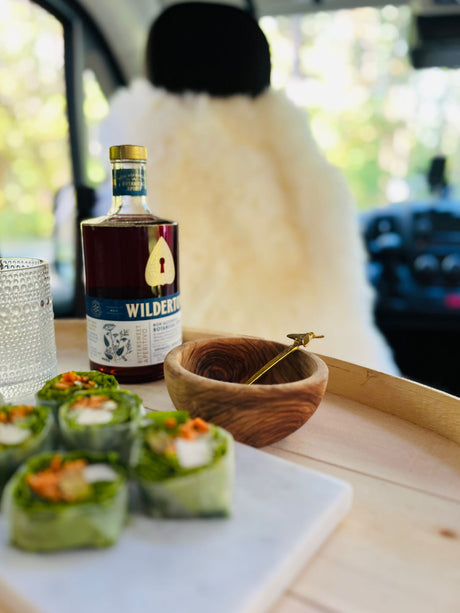 Inside an RV rental, a Wilderton botanical drink and fresh spring rolls offer a refreshing snack on a wooden tray.