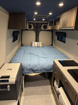 Compact rv rental interior: A cozy bed, mini kitchen with cooktop & sink, Dometic fridge, and overhead storage optimize this camper van.
