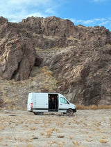 Adventure awaits! White camper van parked against rocky mountains, a person cheering from inside. Ideal rv rental for exploring nature.
